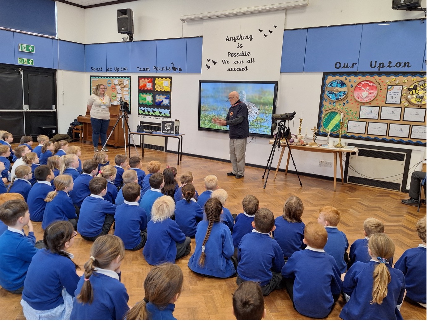 Mike Smart delivering an assembly on Curlews at Upton On Severn Ce Primary School. A photo of a man stood in front of a school group, who are sat on the floor