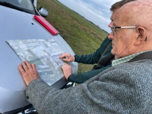 A photo of two men looking at a map laid flat on a car bonnet