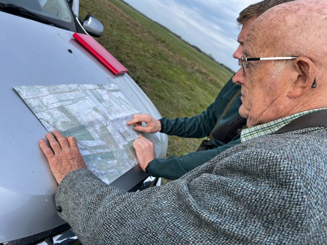 A photo of two men looking at a map laid flat on a car bonnet